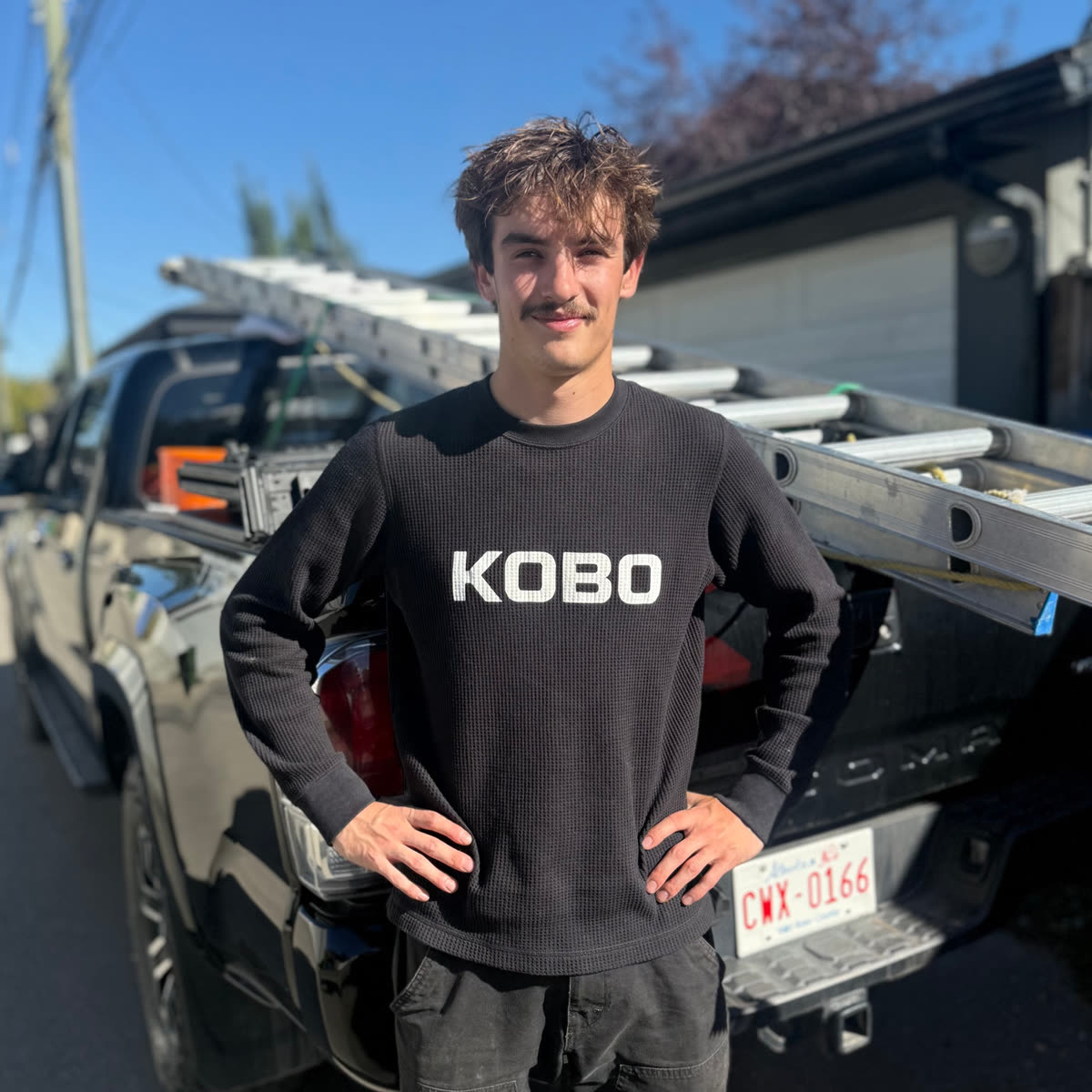 Kobo Exterior Solutions owner in a Kobo crewneck beside the company truck with an extension ladder racked, on a Calgary street
